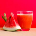 watermelon shake filled glass cup beside sliced watermelon fruit on brown surface